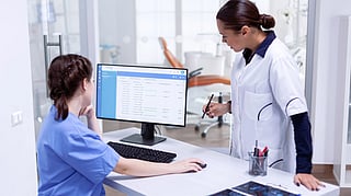 Two healthcare professionals in a clinic setting discuss information on a computer screen. 