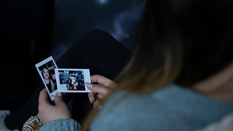 A woman in a blue sweater holds two Polaroid photos, one with a smiling person, the other with a group.