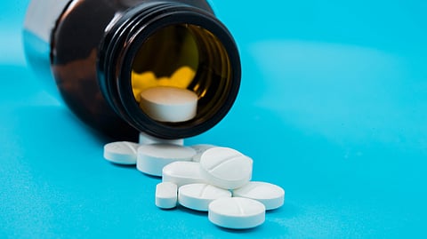A brown pill bottle lies on its side, spilling white round tablets onto a bright blue surface.