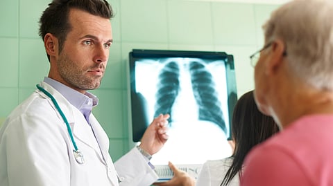 Doctor in a white coat with a stethoscope discusses a chest X-ray with a patient.