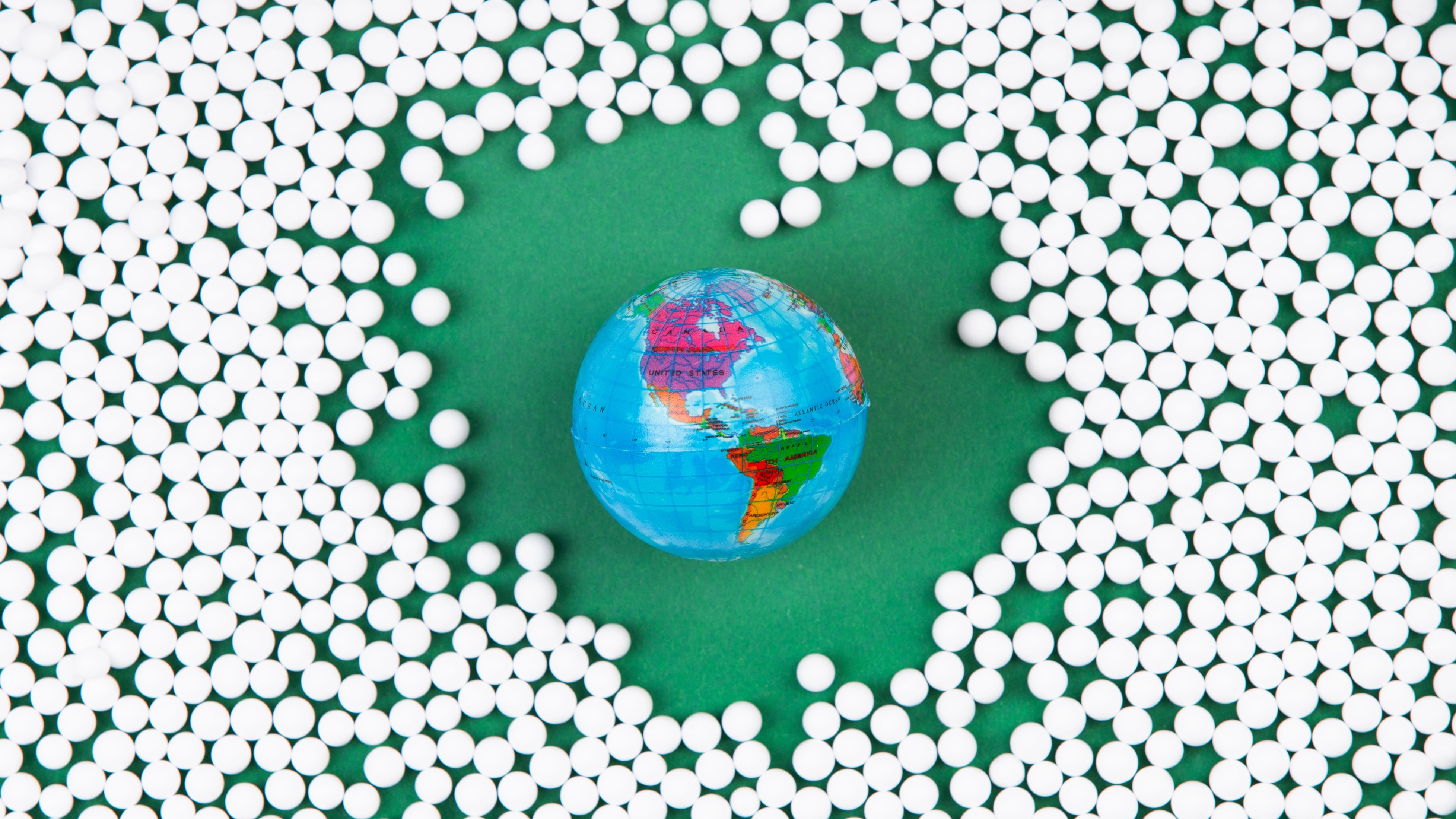 A small, colorful globe is surrounded by scattered white pills on a green background.
