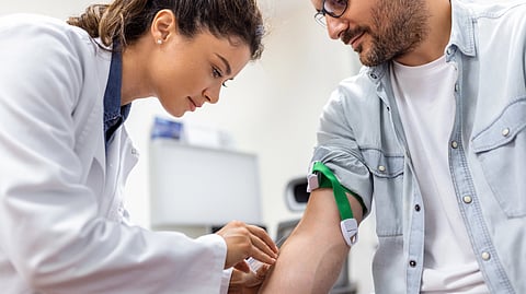 Friendly hospital phlebotomist collecting blood sample from patient in lab preparation for blood test by female doctor medical uniform on the table in white bright room.