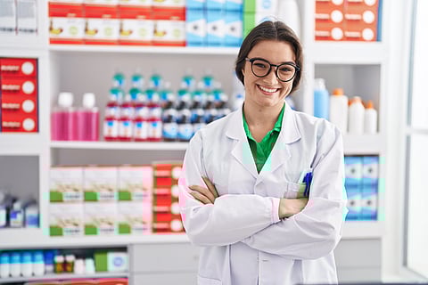 Young hispanic woman pharmacist smiling confident standing with arms crossed at a pharmacy.
