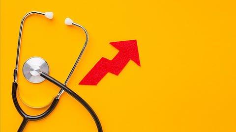 A stethoscope on a yellow background with a red upward arrow showing rising health costs or growth.