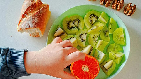 Colorful breakfast with fruit, bread, nuts, and juice, with a hand reaching for the food.