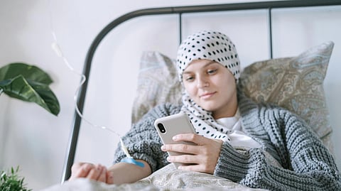 young cancer patient on bed during chemo using phone.