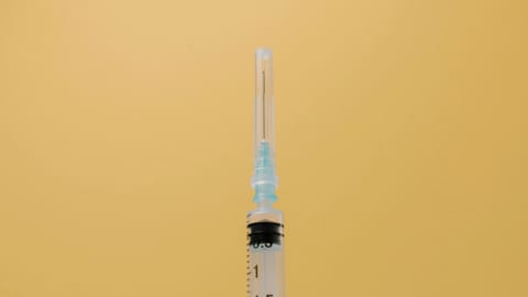 Close-up of a syringe with a blue needle cap, set against a solid yellow background.
