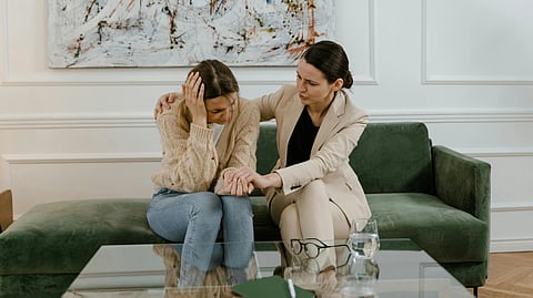 A woman comforts another on a sofa, showing empathy.