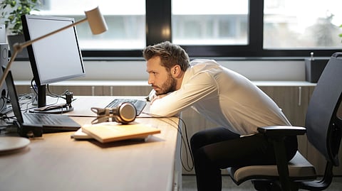 A man in a white shirt leans forward at his desk, focused on his computer.