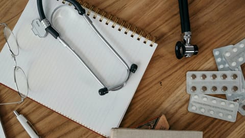 A stethoscope on a notebook with medical tools on a wooden table.
