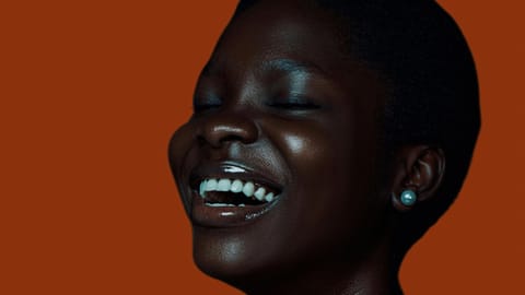 A woman with closed eyes is joyfully laughing against a warm rust-colored backdrop.
