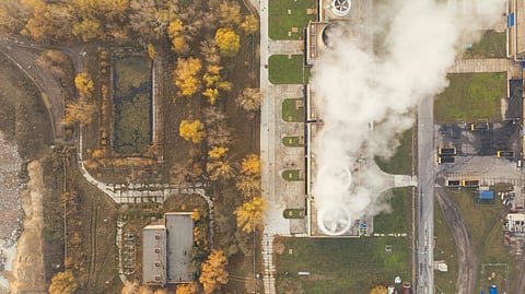 Aerial view of an industrial site with steam rising from cooling towers. Surrounded by roads, trees in autumn colors.