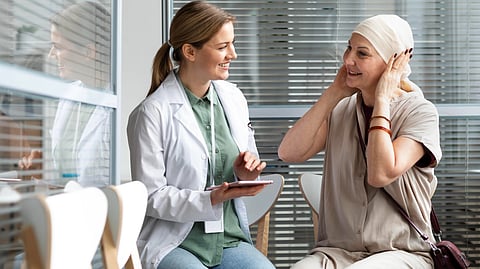 A doctor and a patient sit together smiling. The doctor holds a tablet, and the patient, wearing a headscarf.