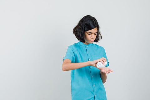 Young lady taking some pills from bottle in blue shirt