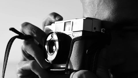Black and white photo of a person holding a vintage camera close to their face, capturing a moment.