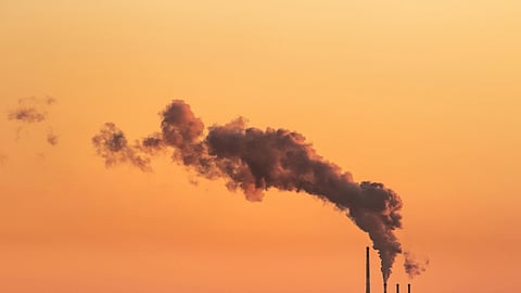 Factory smokestacks releasing thick smoke into a polluted sunset sky.