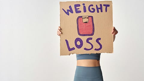 Person holding a cardboard sign with "Weight Loss" and a drawing of a scale.