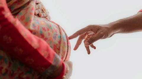 A close-up of a hand gently reaching towards a pregnant belly wrapped in a colorful floral fabric.