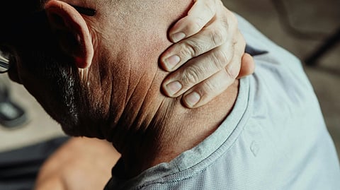 A person in a light-colored shirt grasps the back of their neck with one hand.