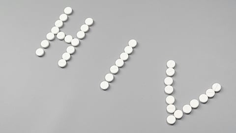 White pills are arranged on a gray surface to spell "HIV." 