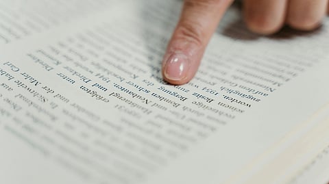 A close-up image of a person's finger tracing text in an open book.