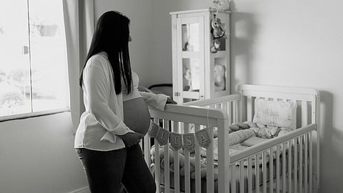 A pregnant woman standing beside a white crib in a softly lit nursery.