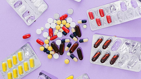 Colorful pills and capsules spill from blister packs onto a purple surface.