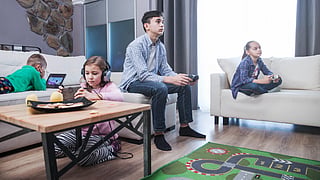 A teenage boy and two girls play video games while another boy uses a tablet.