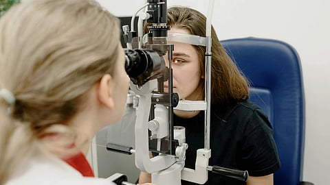 A patient has an eye exam while an optometrist checks their eyes using a slit lamp.