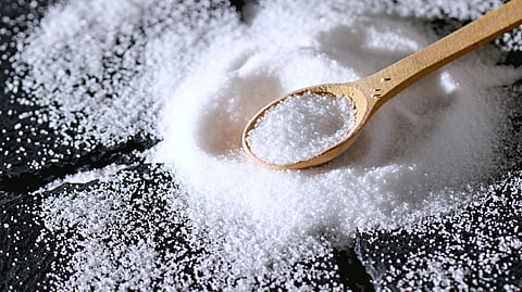 A wooden spoon rests on a pile of coarse salt scattered across a dark surface.