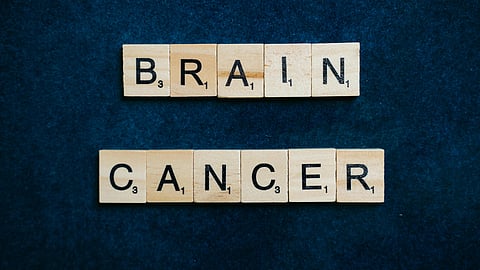 Wooden Scrabble tiles spell "Brain Cancer" on a dark blue background.