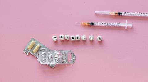 Pills and syringes on a pink background with blocks spelling “DIABETES.”