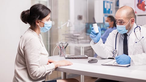 A doctor holds a pill bottle while speaking with a patient in an exam room.