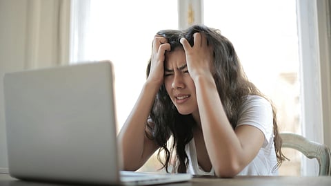 A frustrated woman holding her head while sitting in front of a laptop.