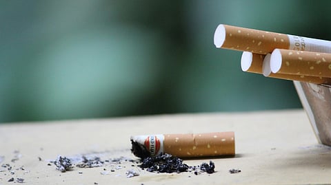 A burnt cigarette with ash beside a nearby cigarette pack.