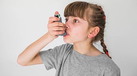 Young girl with braided hair uses an inhaler against a plain white background. 