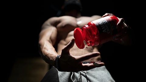 Muscular person pours supplements from a bottle against a dark background.