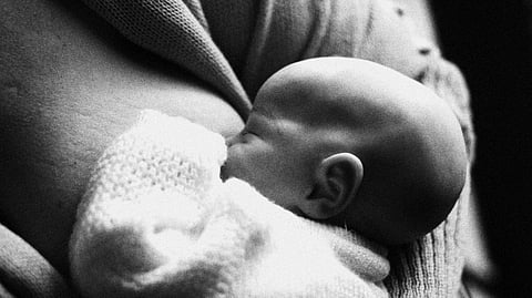 A black-and-white image of a newborn baby nursing.