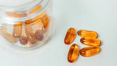 Clear jar with amber gel capsules slightly spilling onto a white surface.