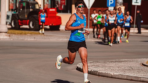 Runner in blue tank top leads a city street race with focus and determination.