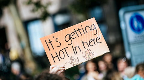 A protest sign held aloft reads "It's getting HOT in here" with flames drawn below. 