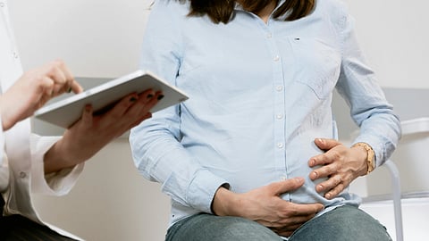 Pregnant woman holds her belly as a healthcare worker takes notes on a tablet.