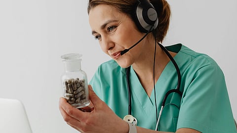 A healthcare worker in scrubs holds medicine during a telehealth video call.
