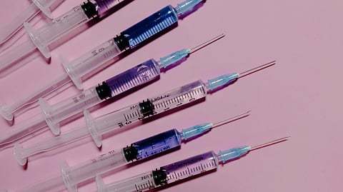 A row of syringes with blue-tinted liquid on a pink background.