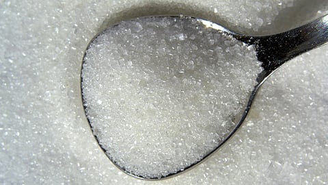 A spoon of white sugar resting on a pile of sugar.