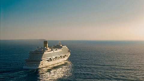 Cruise ship sailing on calm ocean under a clear blue sky, with sunlight reflecting on the water.