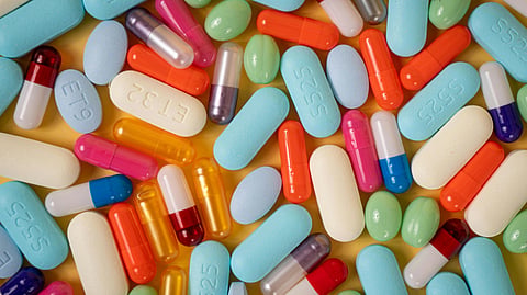 A colorful assortment of various pills and capsules spread across a yellow background.