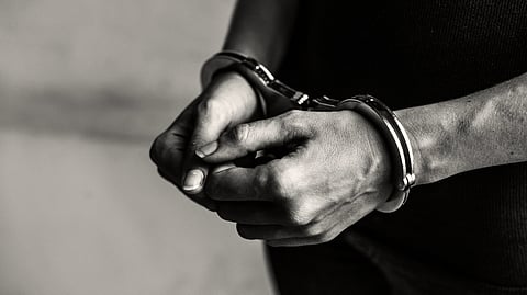 A close-up of a person's hands in handcuffs, against a blurred background. 