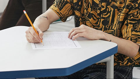  A person writing exam on table and holding pencil and paper.