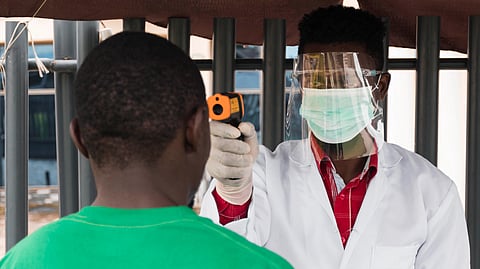 A healthcare worker checks a person’s temperature with a thermometer outdoors.